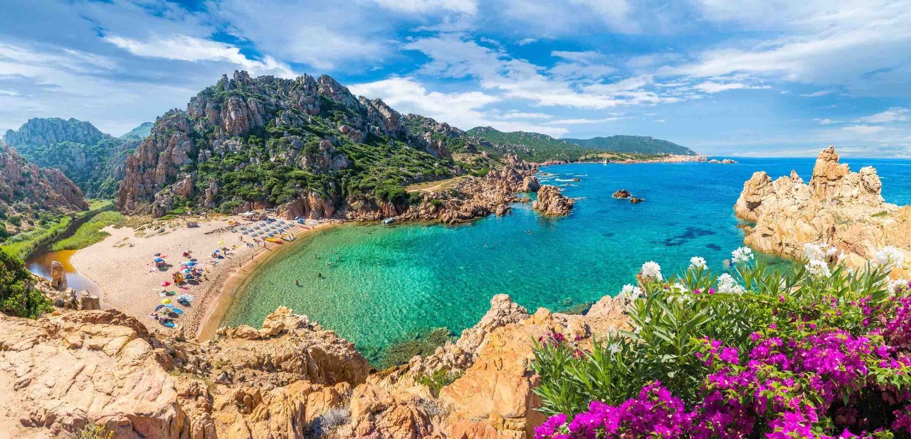 imagem ilustrativa da matéria Um futuro ensolarado: Sardenha, um laboratório verde de transição energética. Na imagem há uma fotografia panorâmica de um cenário de mar e montanhas da ilha da Sardenha, na Itália. 