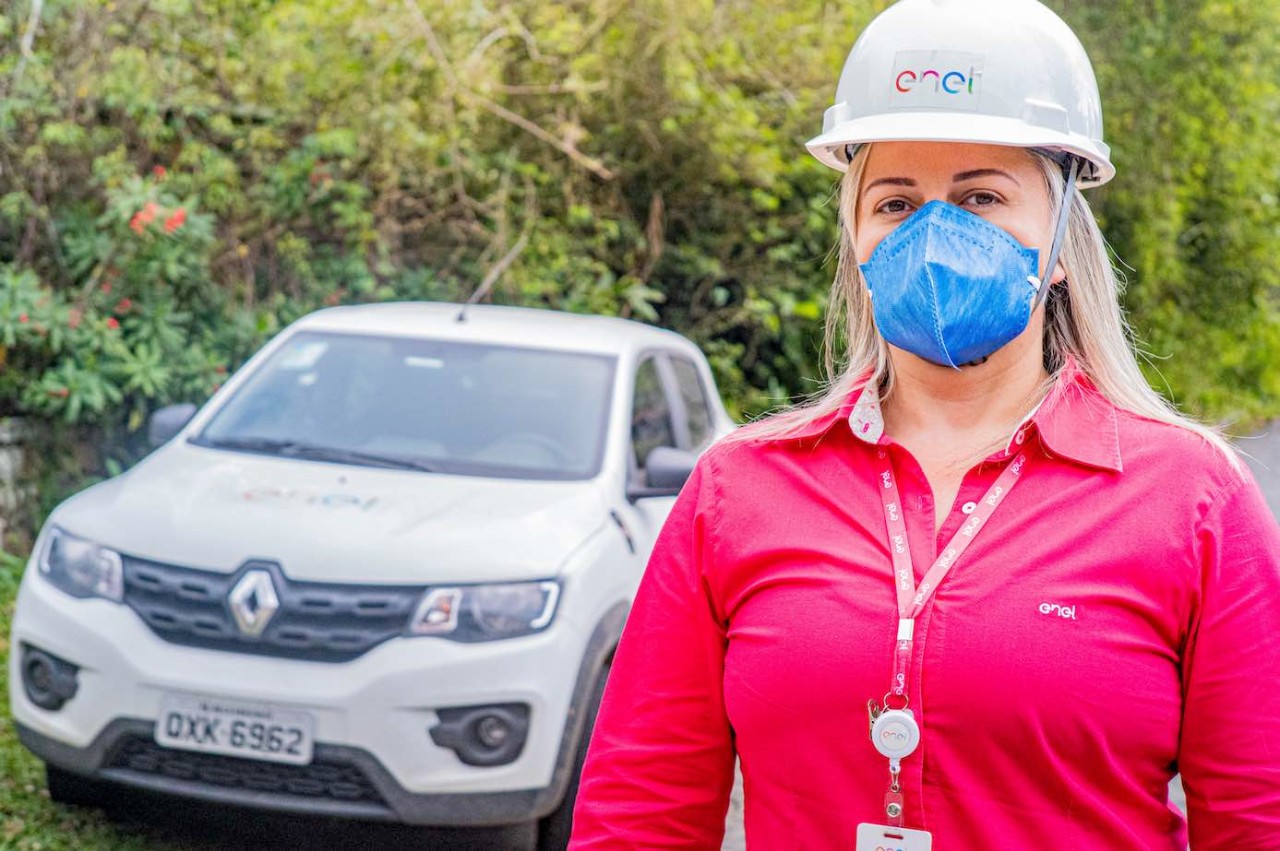 A imagem é uma fotografia da colaboradora Patricia Mota usando máscara protetiva contra a covid na frente do carro da Enel